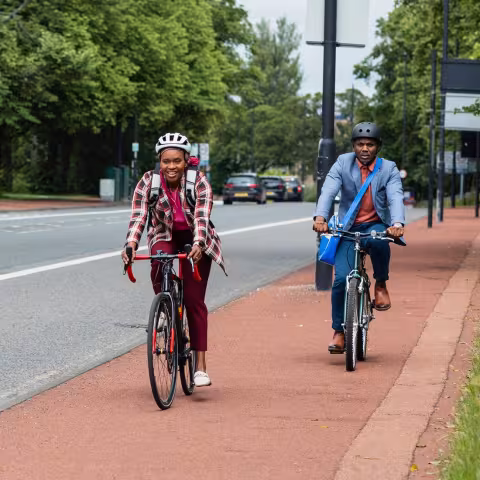Two adults cycling with confidence along a protected cycle lane beside a tree-lined road.
