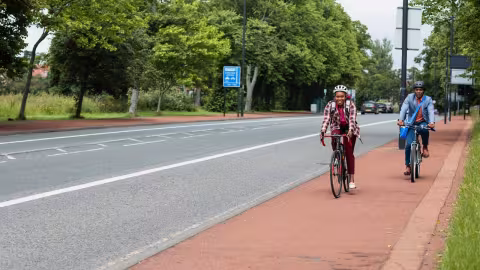 Two adults cycling along a protected cycle lane, shown as a preview of the CycleIn training video.