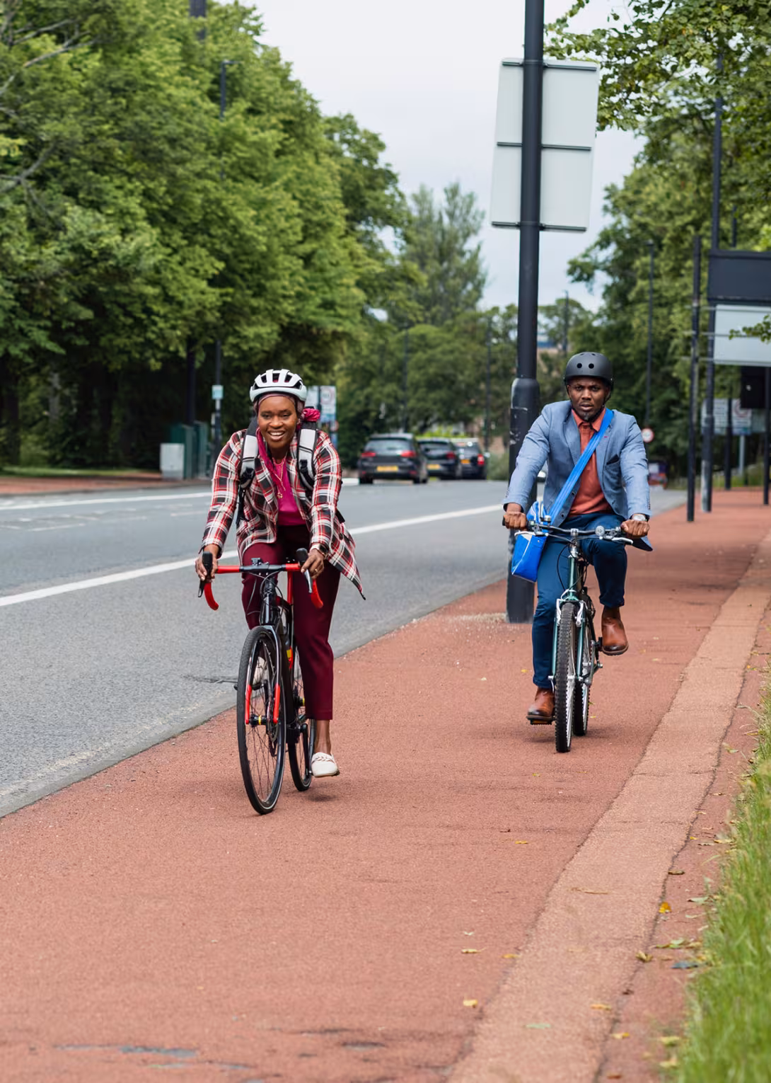 Two adults cycling with confidence along a protected cycle lane beside a tree-lined road.